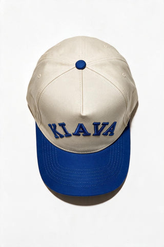 A structured baseball cap with an off-white crown and a royal blue brim, featuring the word 'KIAYA' embroidered in blue across the front. The cap is photographed from a top-down angle on a clean white background.